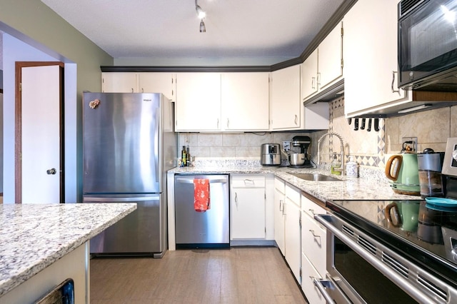 kitchen featuring light stone counters, backsplash, appliances with stainless steel finishes, white cabinetry, and a sink