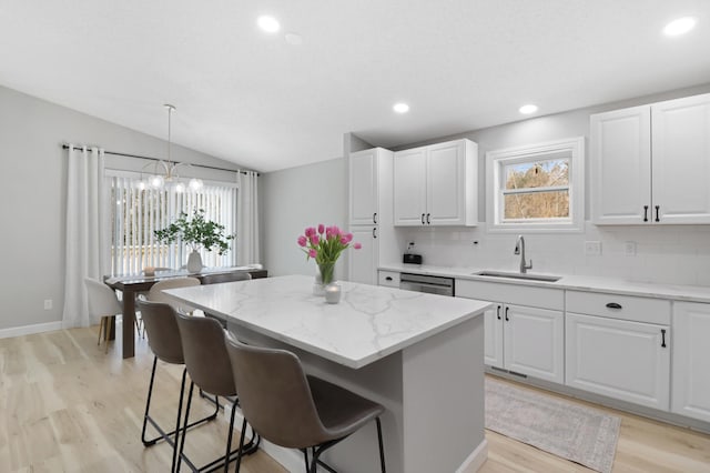 kitchen featuring sink, white cabinetry, decorative light fixtures, a center island, and light stone countertops