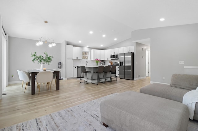 living room with lofted ceiling, sink, a chandelier, and light hardwood / wood-style floors