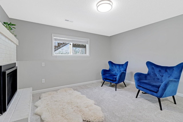 sitting room with a brick fireplace, carpet floors, and a textured ceiling