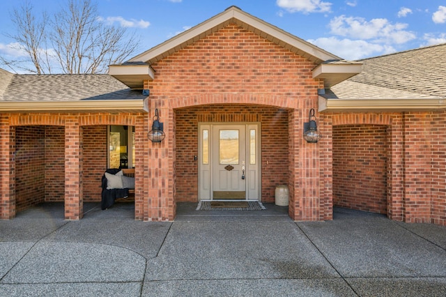 property entrance featuring brick siding and roof with shingles