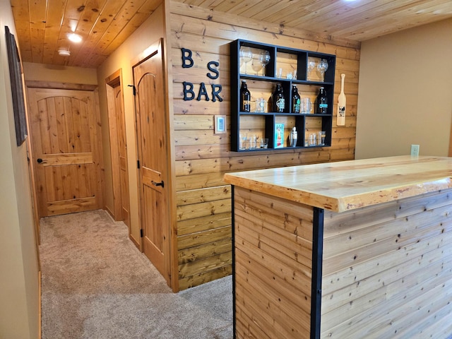 bar with wood walls, wooden ceiling, a bar, and carpet floors