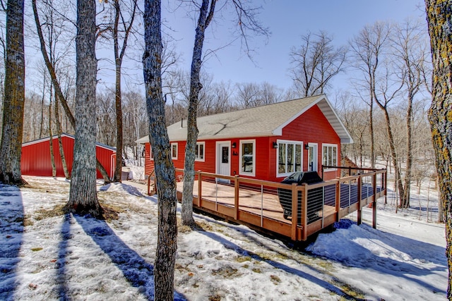 snow covered house featuring a pole building, an outdoor structure, a deck, and roof with shingles