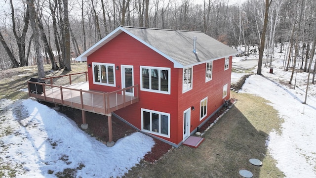 view of snowy exterior featuring driveway, a wooden deck, and a shingled roof