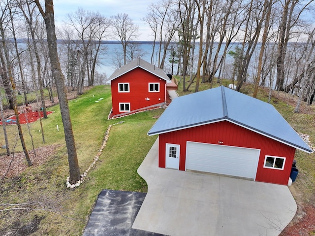 exterior space with a front lawn, a detached garage, an outbuilding, a water view, and concrete driveway
