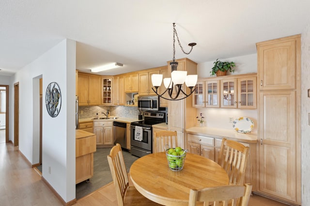 kitchen featuring tasteful backsplash, light brown cabinets, a notable chandelier, pendant lighting, and stainless steel appliances