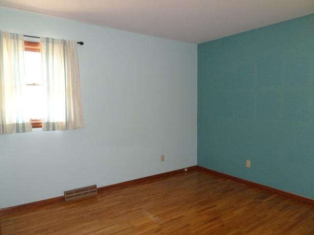 unfurnished room featuring visible vents, baseboards, and wood finished floors