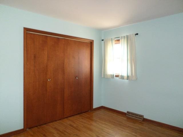 unfurnished bedroom with visible vents, a closet, baseboards, and wood finished floors