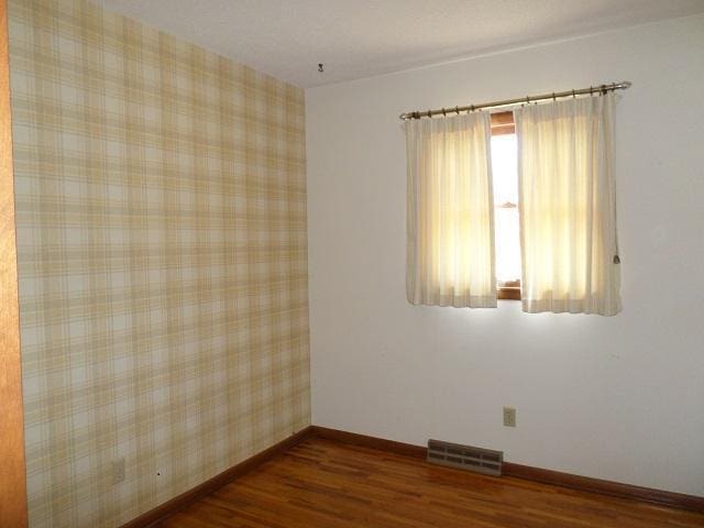 empty room featuring dark wood-type flooring, visible vents, baseboards, and wallpapered walls