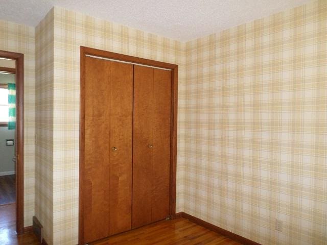 unfurnished bedroom with a closet, baseboards, a textured ceiling, and dark wood-style floors