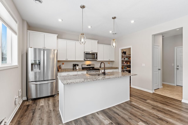 kitchen with stainless steel appliances, an island with sink, hanging light fixtures, and white cabinetry