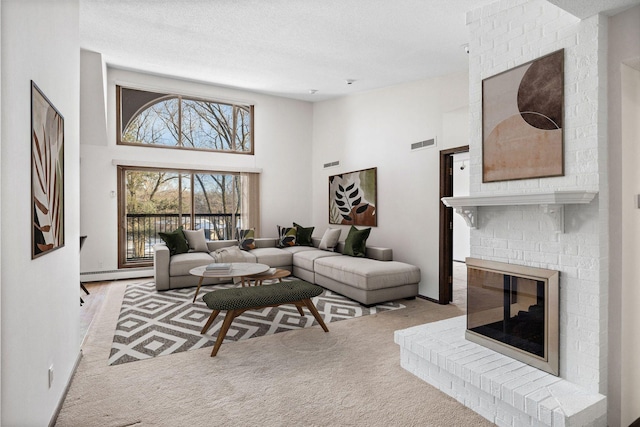 living room with a baseboard heating unit, a towering ceiling, a fireplace, a textured ceiling, and light colored carpet