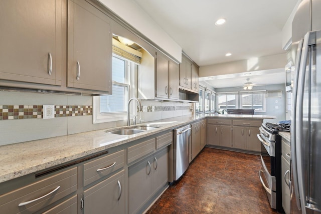 kitchen featuring stainless steel appliances, gray cabinets, backsplash, a sink, and light stone countertops