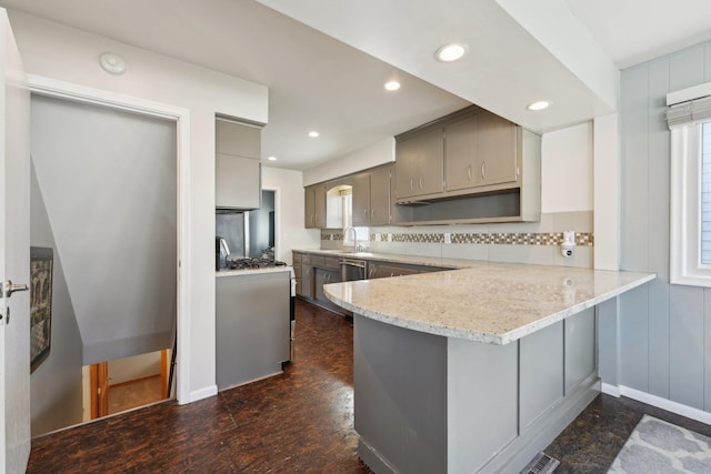 kitchen featuring decorative backsplash, a peninsula, light stone countertops, gray cabinets, and a sink