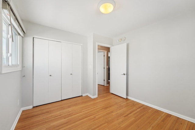 unfurnished bedroom featuring light wood-type flooring, baseboards, and a closet