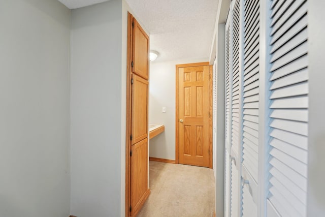 corridor with light carpet, a textured ceiling, and baseboards