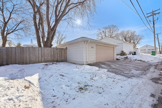 snow covered garage featuring a detached garage and fence