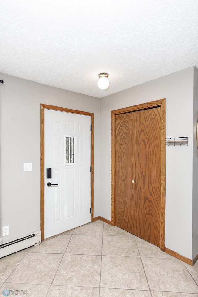 entryway featuring a baseboard heating unit, baseboards, light tile patterned floors, and a textured ceiling