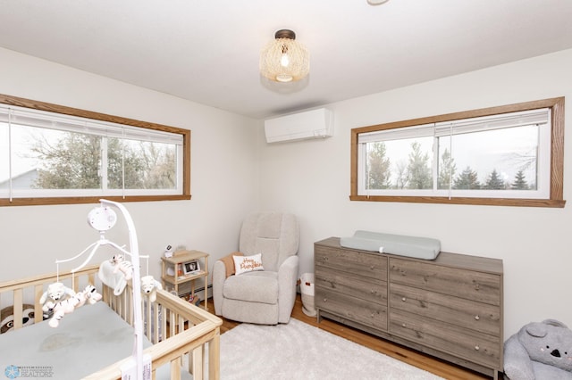 bedroom featuring multiple windows, an AC wall unit, a nursery area, and wood finished floors