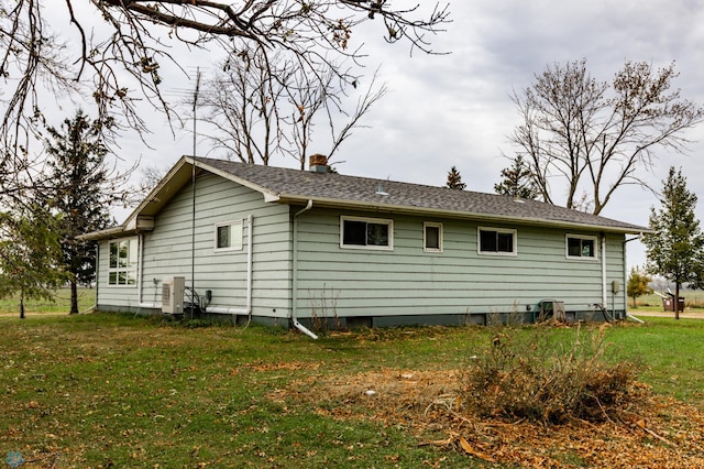 back of house with a lawn, a chimney, and a shingled roof