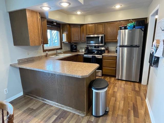 kitchen featuring hardwood / wood-style floors, sink, kitchen peninsula, and appliances with stainless steel finishes