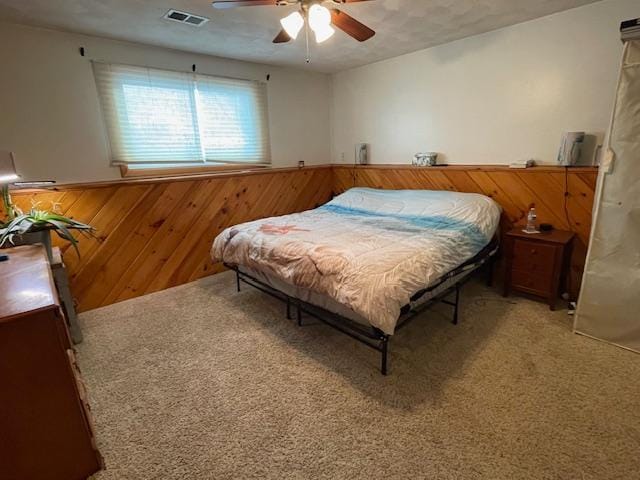 bedroom featuring ceiling fan, wooden walls, and carpet