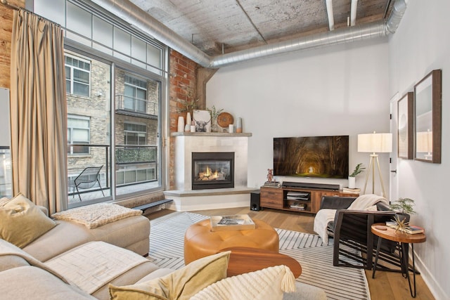 living room featuring brick wall, a fireplace, baseboards, and wood finished floors