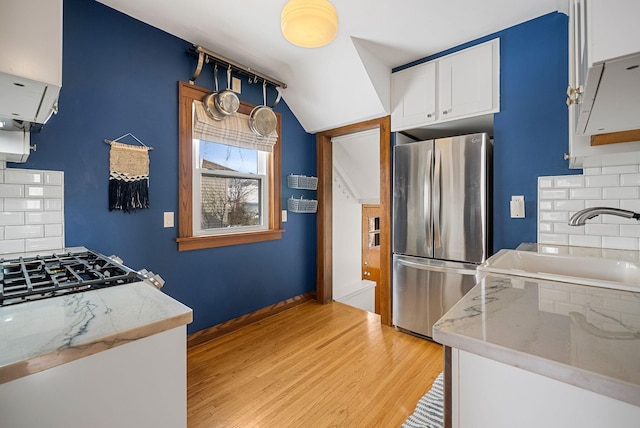 kitchen with sink, white cabinets, stainless steel fridge, decorative backsplash, and light hardwood / wood-style floors