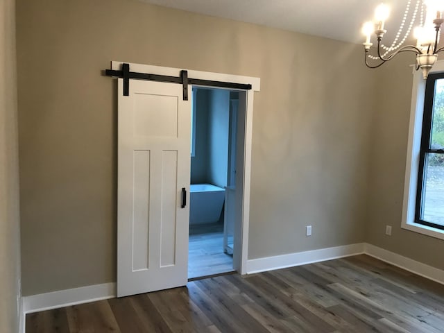 spare room with dark hardwood / wood-style floors, a chandelier, and a barn door