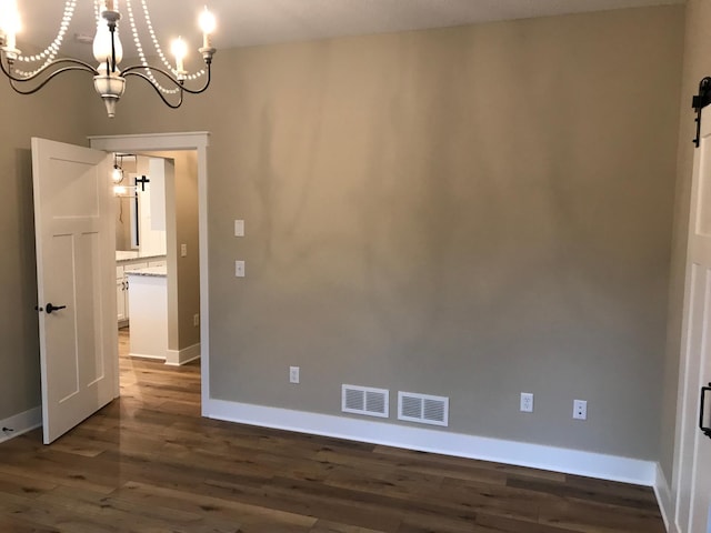 spare room with a barn door, dark hardwood / wood-style flooring, and a chandelier