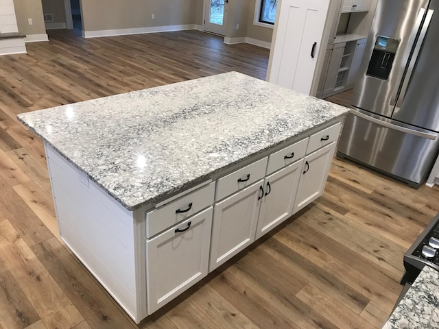 kitchen featuring stainless steel refrigerator with ice dispenser, light stone countertops, a kitchen island, and white cabinets