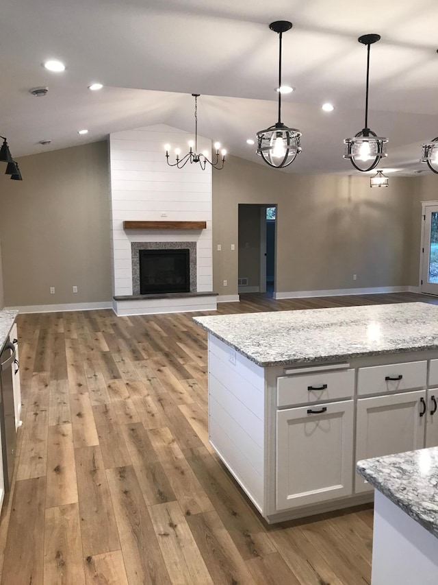 kitchen featuring pendant lighting, lofted ceiling, white cabinets, light stone counters, and light hardwood / wood-style flooring