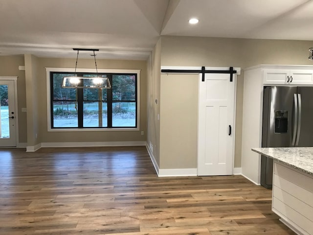 kitchen featuring white cabinetry, hanging light fixtures, light stone counters, stainless steel fridge with ice dispenser, and a barn door