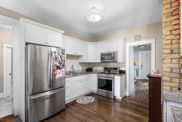 kitchen with appliances with stainless steel finishes, white cabinets, a sink, and light stone counters