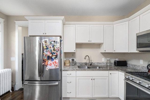 kitchen with dark stone counters, white cabinets, radiator, stainless steel appliances, and a sink