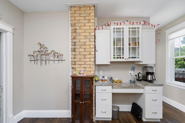 kitchen featuring dark wood-style flooring, white cabinetry, baseboards, light stone countertops, and glass insert cabinets