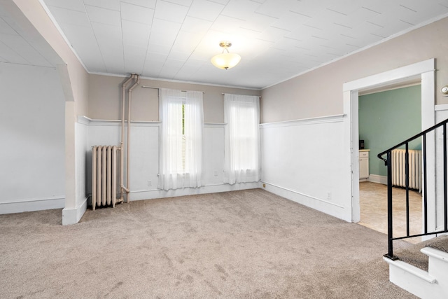 unfurnished room with light colored carpet, radiator, a wainscoted wall, ornamental molding, and stairs