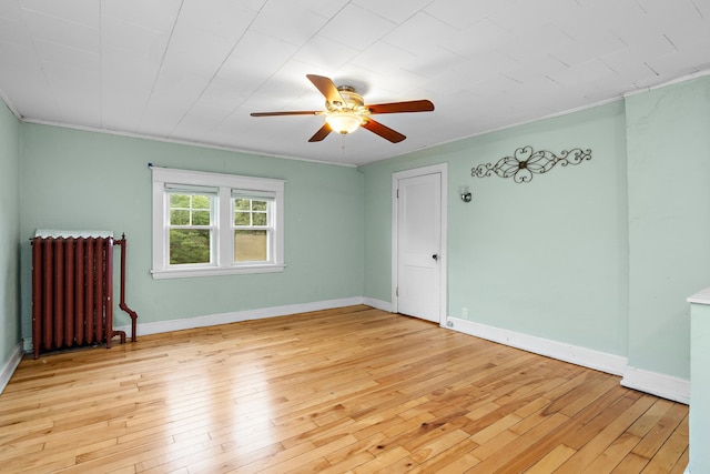 empty room with a ceiling fan, radiator, light wood-style flooring, and baseboards