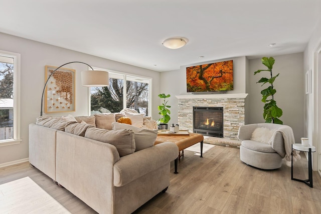 living room featuring wood-type flooring, a stone fireplace, and a wealth of natural light