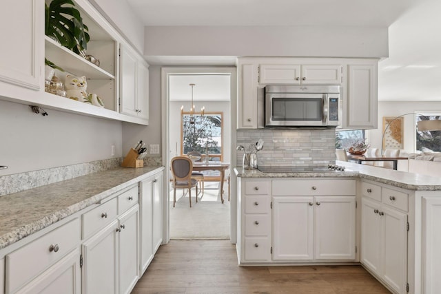 kitchen with tasteful backsplash, black electric stovetop, light wood-type flooring, and white cabinets