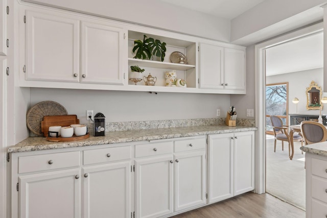 bar with white cabinets, light stone counters, and light hardwood / wood-style flooring