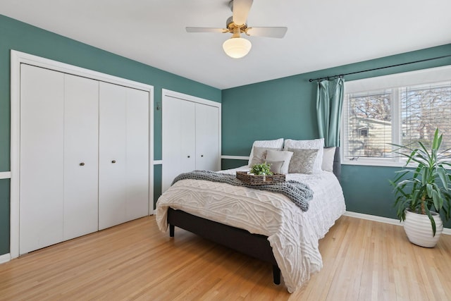 bedroom featuring ceiling fan, light hardwood / wood-style flooring, and two closets