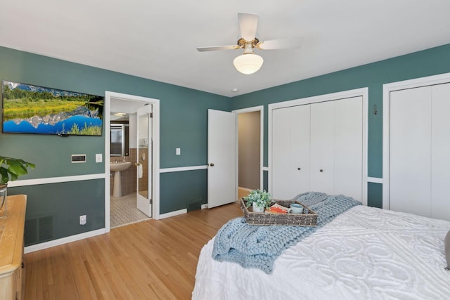 bedroom featuring sink, ceiling fan, ensuite bathroom, wood-type flooring, and two closets