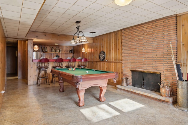 game room featuring a brick fireplace, bar area, wooden walls, and billiards