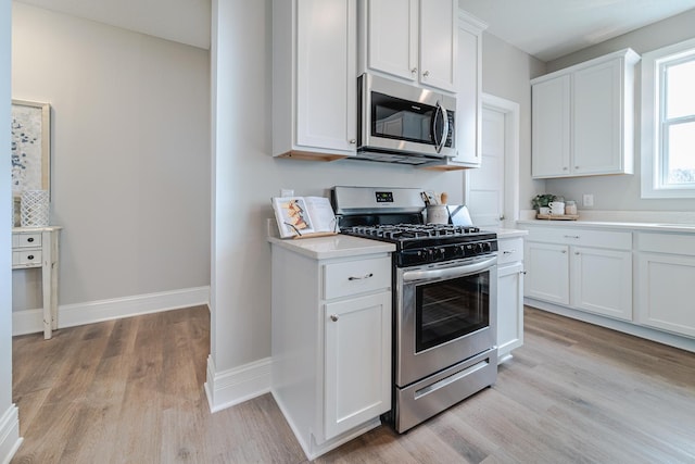 kitchen with stainless steel appliances, white cabinetry, and light hardwood / wood-style floors