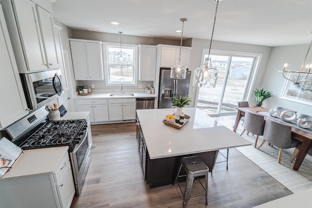 kitchen with sink, white cabinetry, hanging light fixtures, stainless steel appliances, and a center island