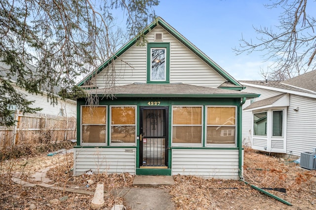 view of front facade with a sunroom, roof with shingles, fence, and central air condition unit