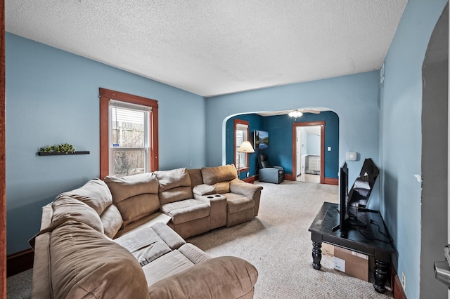 living area featuring arched walkways, a textured ceiling, carpet, and a ceiling fan