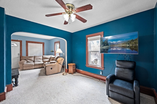 living area with arched walkways, carpet flooring, ceiling fan, and a textured ceiling