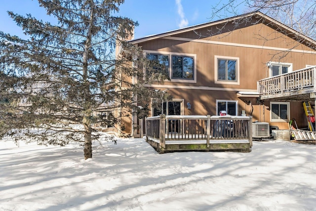 snow covered back of property with central air condition unit and a wooden deck